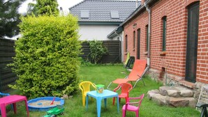 A backyard with a brick house, a green bush, a small pool, and colorful plastic chairs and tables.