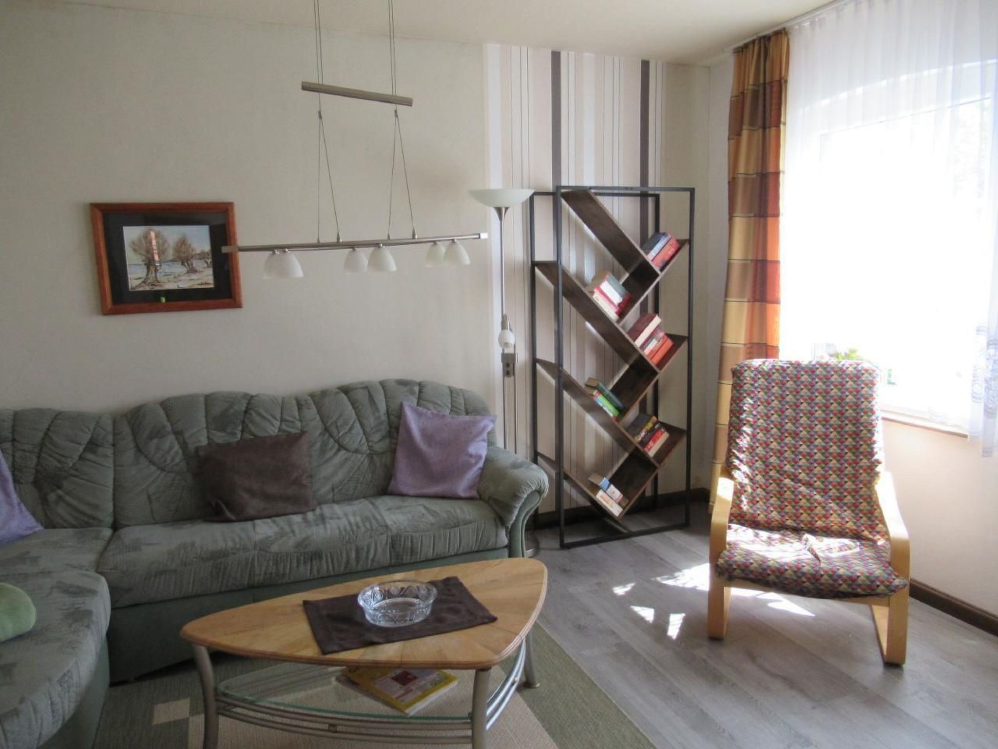 A living room with a sofa, a coffee table, a bookshelf, and a patterned armchair.