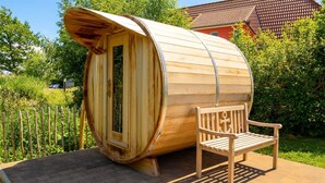 A sauna in the shape of a wooden barrel with a bench inside, set on a paved area with a wooden fence and greenery in the background. - Marvin in Beckerwitz by Interhome (Alt Jassewitz)