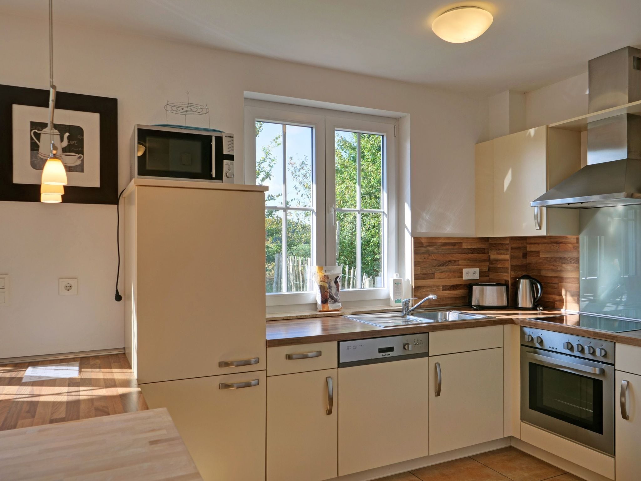 A modern kitchen with white cabinetry, a built-in microwave, a dishwasher, a stove, and a window providing natural light.