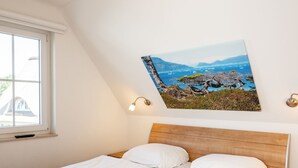 Ein Schlafzimmer mit einem hölzernen Kopfende, weißer Bettwäsche, einem Landschaftsbild und einer Nachttischlampe.