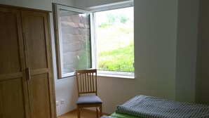 Een slaapkamer met een houten kledingkast, een enkele stoel en twee bedden met groene beddengoed.