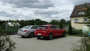 Dos coches aparcados en una entrada con una casa y vegetación al fondo.