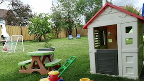 Un área de juegos infantiles con un cobertizo pequeño, una mesa de picnic y diversos juguetes.