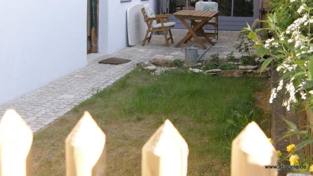 A patio with a table and chairs, a small garden area, and a white building with windows. - Ferienhaus by Interhome (Schernfeld)