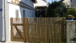 A white building with a wooden fence, a stone pillar with a planter, and a clear sky. - Ferienhaus by Interhome (Schernfeld)