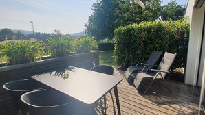 Eine Holzdiele mit Tisch und Stühlen, umgeben von Grün und Blick auf die Landschaft.
