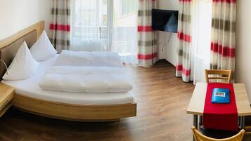 Ein Hotelzimmer mit Bett, Fernseher, Esstisch mit roter Tischdecke und Holzboden.