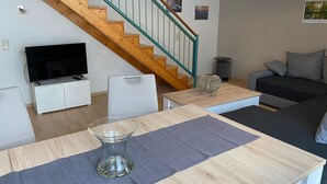 Una sala de estar moderna con una escalera de madera, un televisor de pantalla plana, un sofá y un comedor con mesa de vidrio.