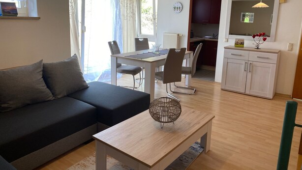 Una sala de estar moderna con sofá, mesa de comedor, sillas y una cocina con alacenas y lavamanos.