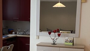 Una cocina con un armario blanco, una lámpara colgante y un jarrón con flores rojas.