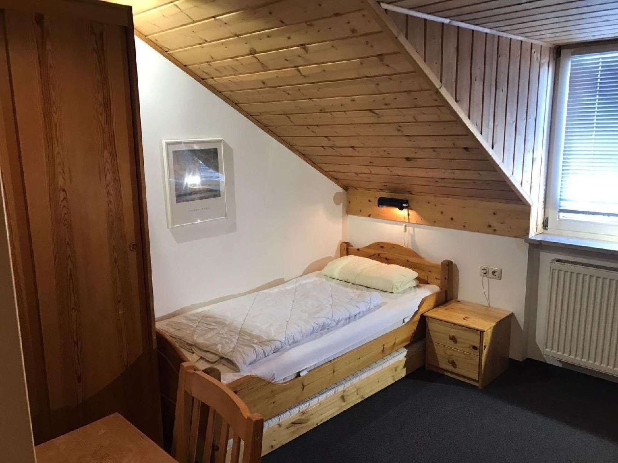 Une petite chambre à coucher accueillante, avec un plafond en pente, un lit simple, une table de chevet, une chaise et un radiateur.
