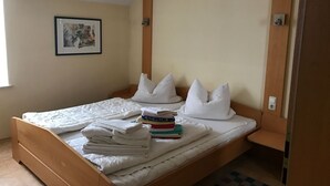 A single bed with a wooden frame, white bedding, and pillows. There is a framed picture on the wall, a small table beside the bed, and a checkered rug on the floor. - Ferienresidenz by Interhome (Bad Kötzting)