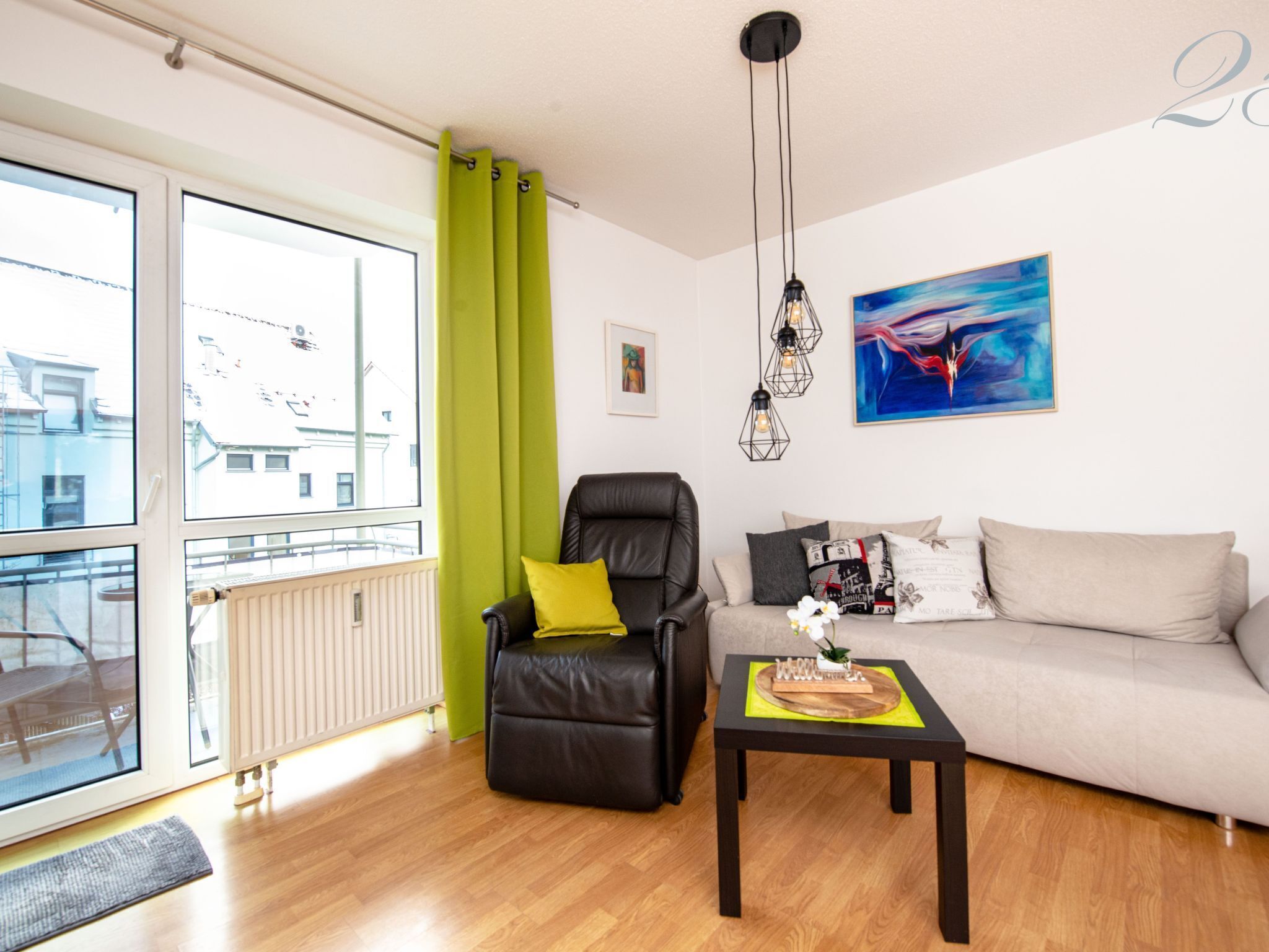 Ein modernes Wohnzimmer mit Ledersessel, Sofa und Couchtisch. Es gibt ein großes Fenster mit Vorhängen, eine Heizung und ein Bild an der Wand.