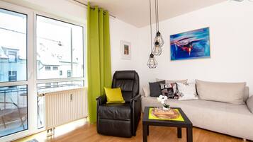 Ein modernes Wohnzimmer mit Ledersessel, Sofa und Couchtisch. Es gibt ein großes Fenster mit Vorhängen, eine Heizung und ein Bild an der Wand.