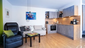 Un salon moderne avec un canapé en cuir noir, un canapé blanc et une table basse. Il y a également un coin cuisine équipé d’un four à micro-ondes, d’une cuisinière et de placards.