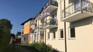 Un edificio residenziale a più piani con balconi, un ingresso carrabile e cielo sereno.