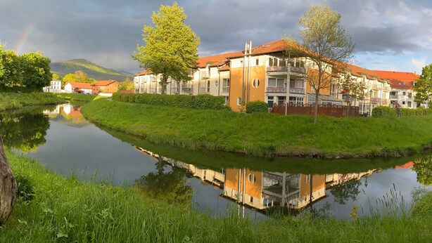 Una vista sul fiume di una zona residenziale con edifici a più piani, un fiume tranquillo e un arcobaleno nel cielo.
