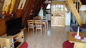 A cozy living room with a TV, wooden furniture, a kitchen in the background, and a staircase. - Haus am See mit Fasssauna, Liegewiese und Grill by Interhome (Waldkirchen)