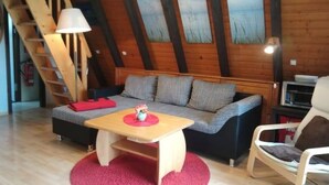A cozy loft-style room with a wooden ceiling, a sofa, a chair, a small table, and a red rug. - Haus am See mit Fasssauna, Liegewiese und Grill by Interhome (Waldkirchen)