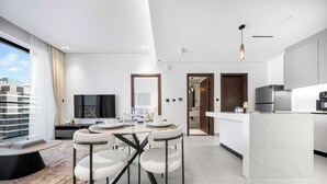 Een moderne keuken met een marmeren kookeiland, een eethoek met een ronde tafel en stoelen, en een groot raam met gordijnen.