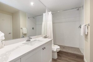 Een moderne badkamer met een grote spiegel, een wit wastafelmeubel en een douchehoek.