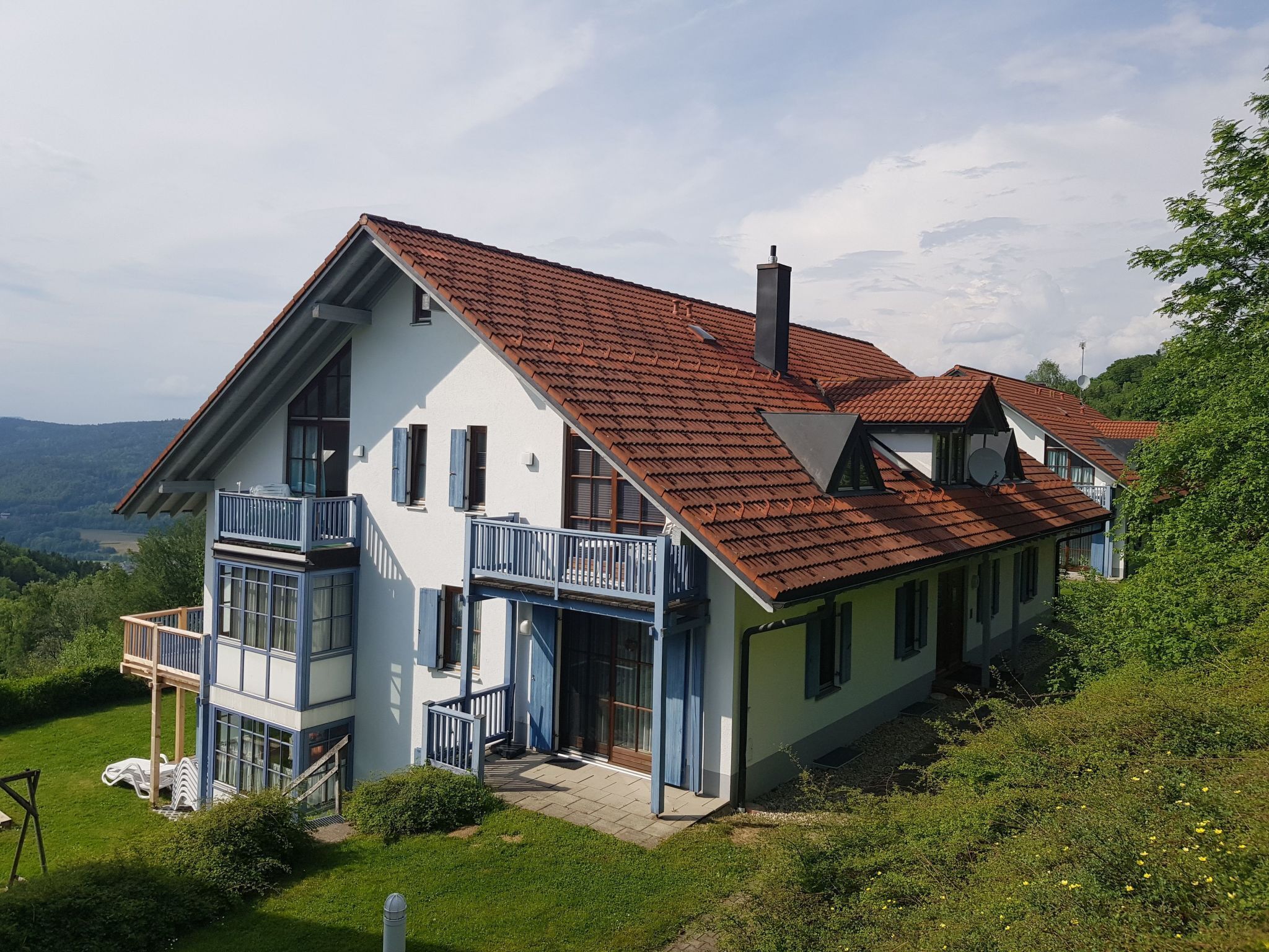 Une maison à deux étages, avec un toit recouvert de tuiles rouges, un balcon et une vue sur le paysage environnant.