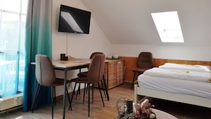 Ett modernt rum med en säng, ett skrivbord med stolar, en TV och ett takfönster.