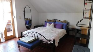 Een slaapkamer met een bed, een bankje, een spiegel en een metalen schapkas.