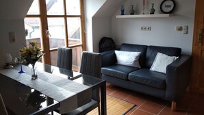 Een woonkamer met een glazen tafel, een blauwe bank en een raam met uitzicht op gebouwen.