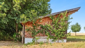 Un rustico chalet in legno con tetto spiovente, circondato da fitta vegetazione e una panchina di fronte.
