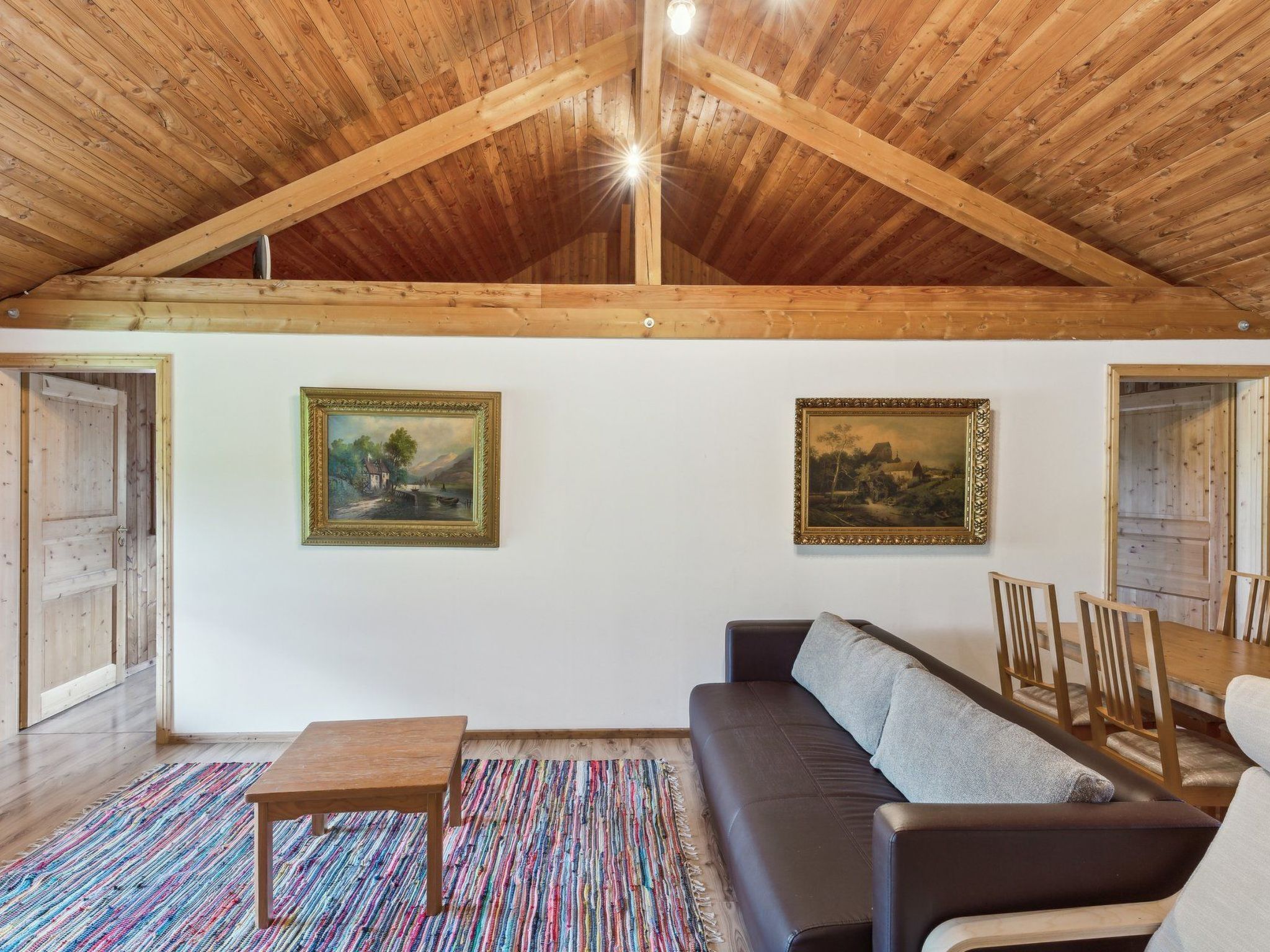 Una habitación acogedora con vigas de madera, un sofá negro, una mesa de madera y dos cuadros enmarcados en las paredes.