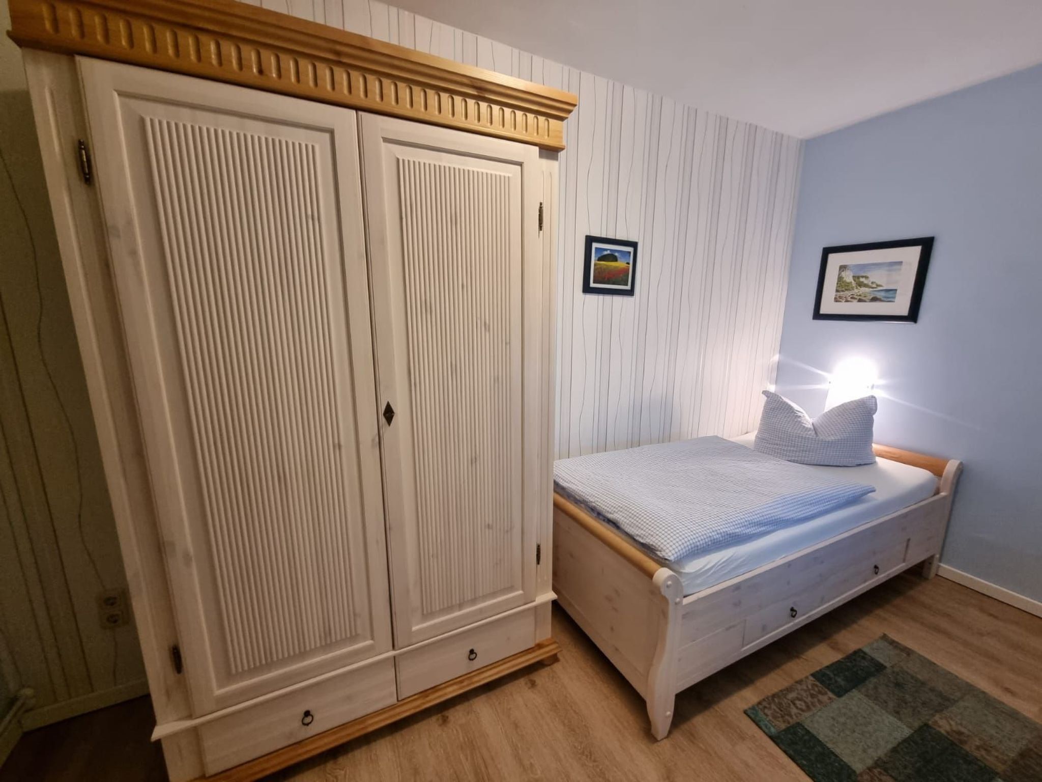 Une chambre à coucher avec un lit en bois, une armoire et deux tableaux encadrés accrochés au mur.
