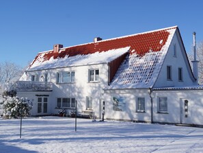 Een huis met twee verdiepingen, een rode dakbedekking, witte muren en een voortuin met een bankje.