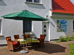 Een terras met een tafel en stoelen, een groene parasol, en een schilderij van een strand.