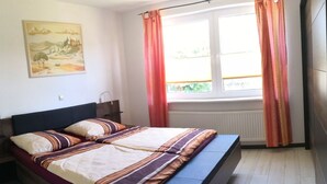Een slaapkamer met een bed, een nachtkastje, een raam met gordijnen en een schilderij aan de muur.