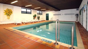 Piscina interna com piso ladrilhado, cadeiras de descanso e teto de madeira.