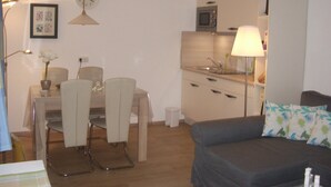 Espaço compacto com cozinha compacta, área de refeições com mesa e cadeiras, e sofá com almofada floral.