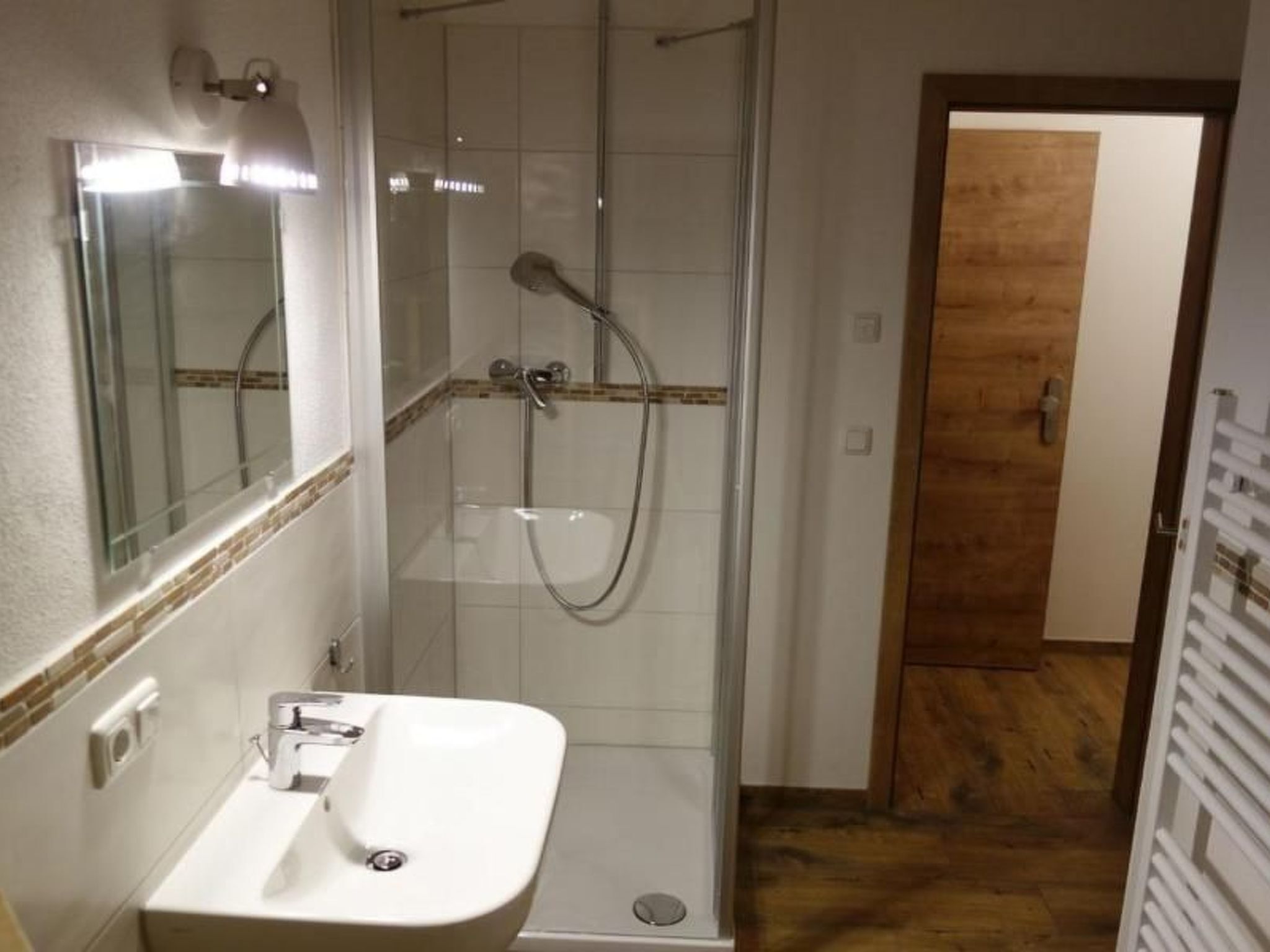 A bathroom with a glass-enclosed shower, a white sink, and a wooden door leading to another room.