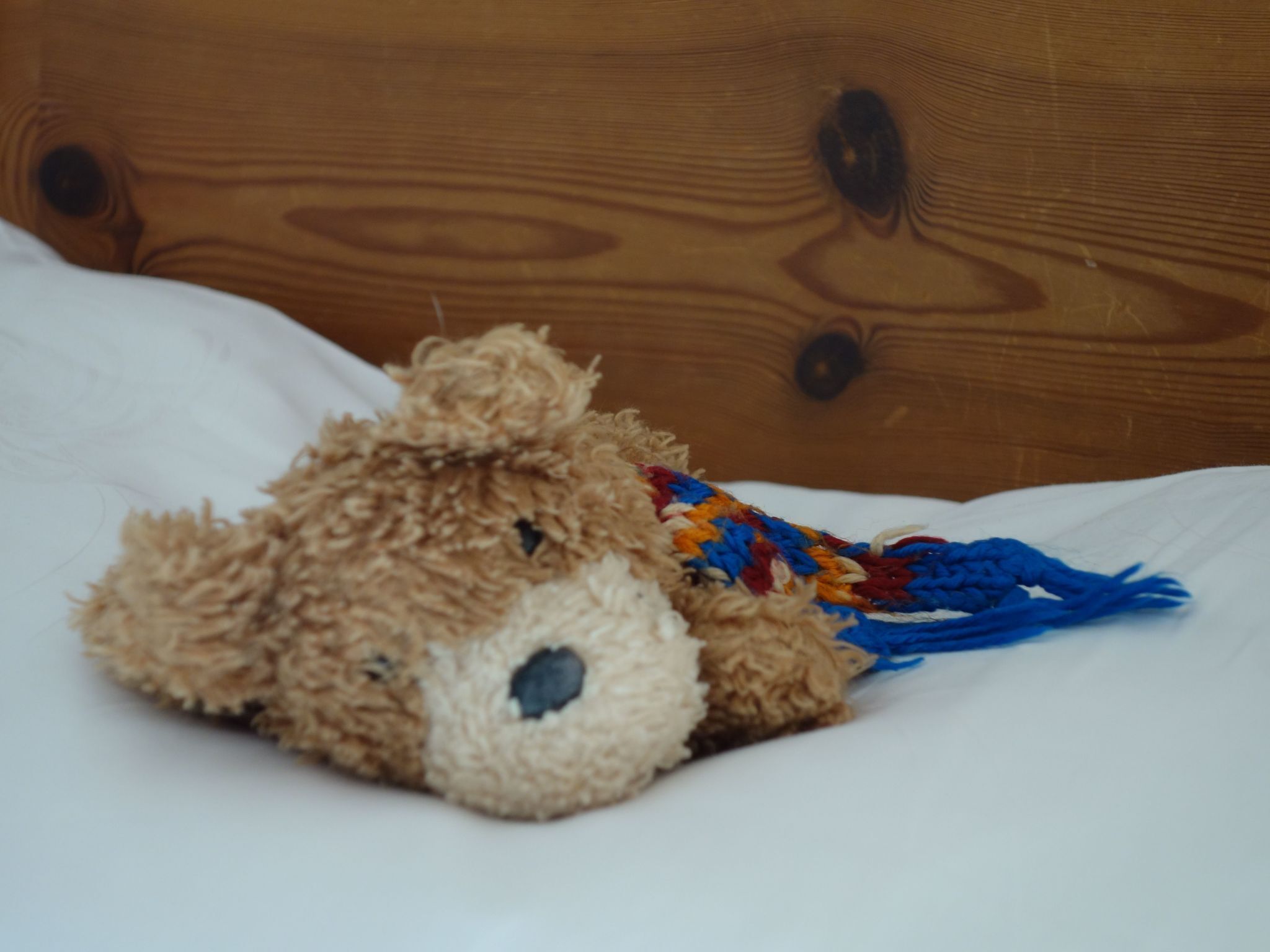 Een zacht knuffeldiertje op een bed met een houten hoofdeinde.