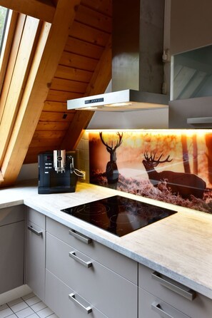 Eine moderne Küche mit Einbauherd, Holzbalkendecke und einer Spritzschutzleiste mit Hirschmotiv.
