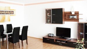 En moderne stue med et fladskærms-tv, et sofabord og et spiseområde med stole.