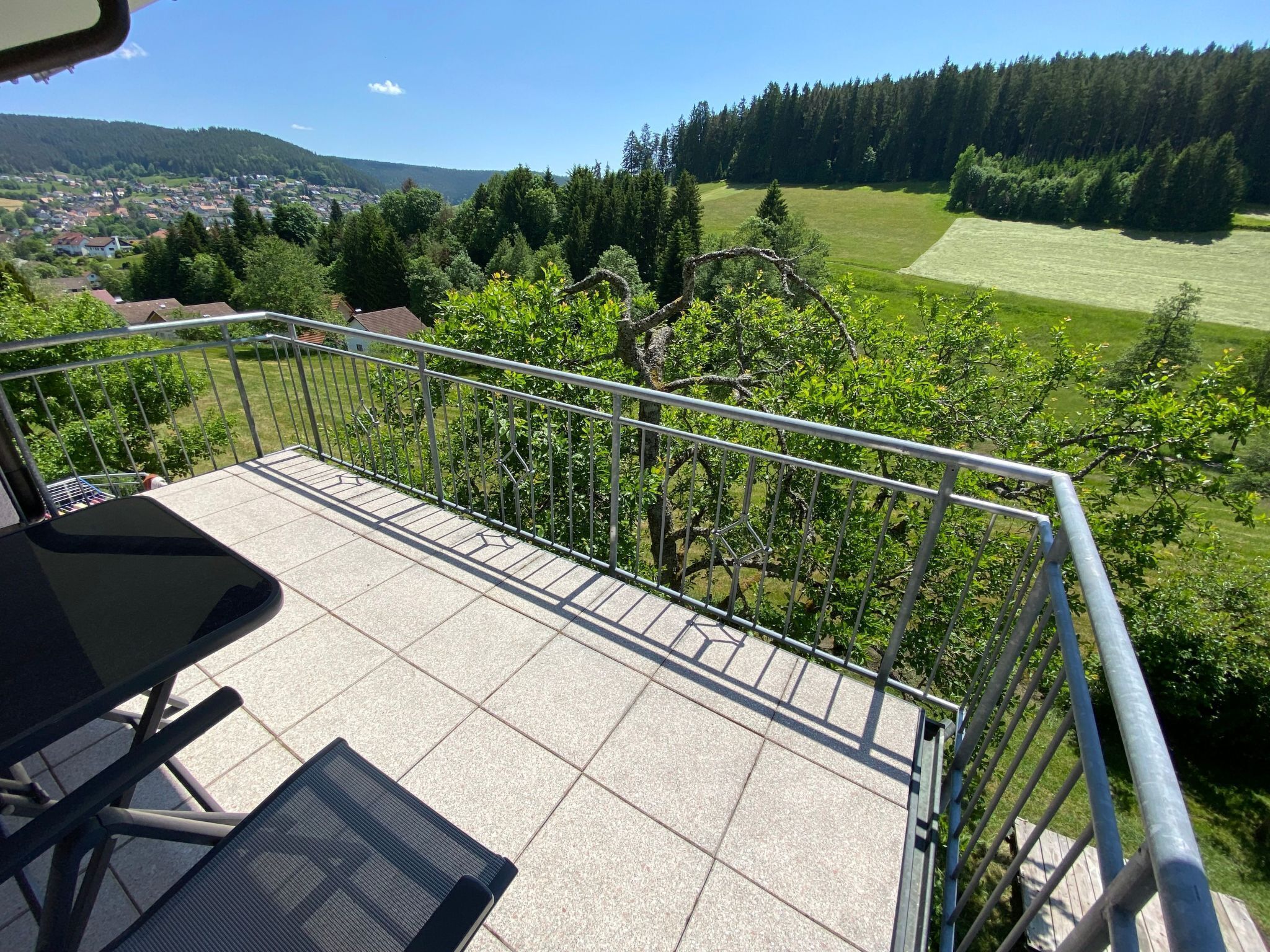 Un balcon offrant une vue sur un paysage verdoyant, avec des arbres et un village situé au loin.