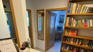 Zona de recepción de un hotel con un mostrador de madera, un cartel de bienvenida, una estantería llena de libros y suelo de baldosas.