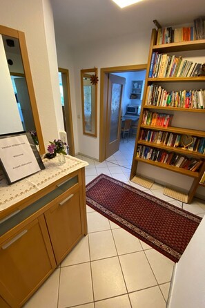 Ein Hotel-Empfangsbereich mit einem Holztisch, einem Willkommen-Schild, einem Bücherregal voller Bücher und einem gefliesten Boden.