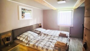 Ein Schlafzimmer mit einem Bett, einem Nachttisch, einer Wandlampe, einem Fenster mit Jalousien und einem gerahmten Bild an der Wand.