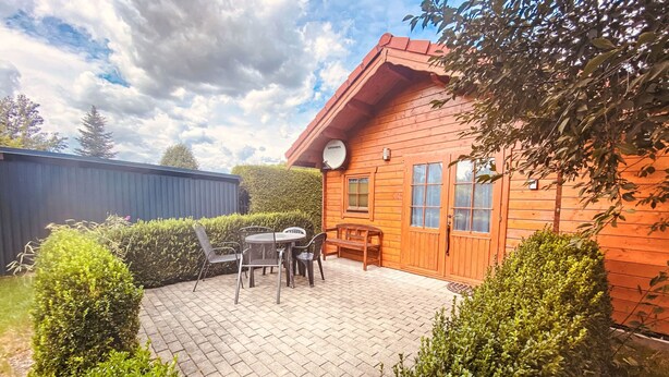 Eine Holzhütte mit Terrasse, Tisch und Stühlen sowie einer Bank.