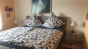 A neatly made bed with patterned bedding, two bedside lamps, a framed picture above the bed, and a small table with a lamp beside the bed. - Schöndorf by Interhome (Tholey)