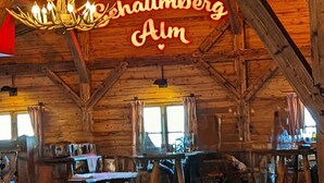 A rustic wooden interior with a chandelier, tables, and a sign reading "Schauberg Alm". - Schöndorf by Interhome (Tholey)