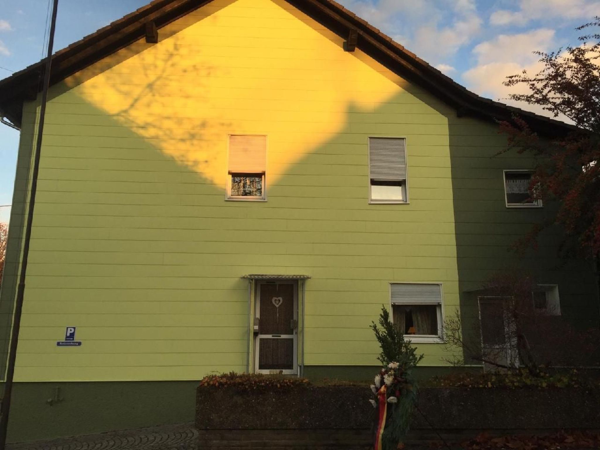 A two-story building with a green facade, a small front porch, and a visible garage door.